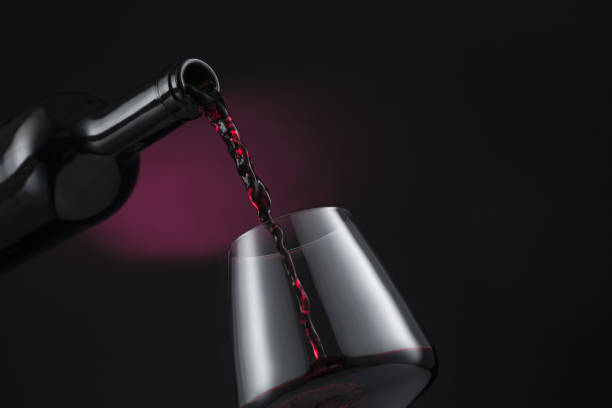 bouteille de vin rouge versée dans le verre de vin, sur fond noir et rouge. - shot glass glass black empty photos et images de collection