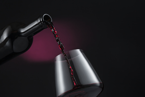 Bottle of red wine poured into the wine glass, on black and red background.