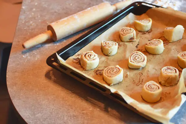 Homemade unbaked cinnamon bans rolls in baking pan on kitchen table.