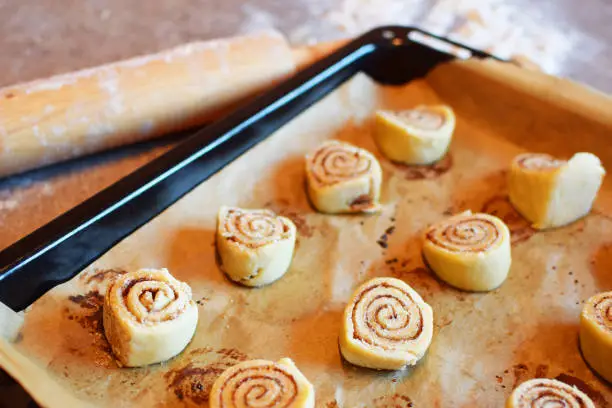 Homemade unbaked cinnamon bans rolls in baking pan on kitchen table.