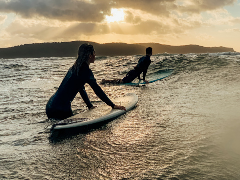 A shot of a young man and woman wearing wetsuits, they are surfing on the sea.