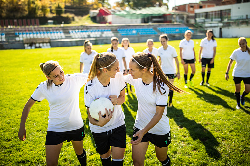 Young female soccer team celebrating a goal, smiling and embracing on soccer field during sunny summer day