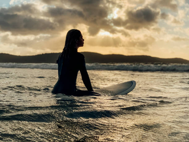 A shot of a young woman wearing a wetsuit, she is surfing on the sea.