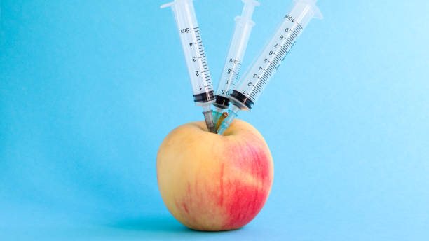 three different medical syringes sticking deep into an apple on a blue background. the fruit is strewn with syringes. a ripe red apple pierced from all sides by syringes. healthcare or cosmetology - injecting healthy eating laboratory dna imagens e fotografias de stock