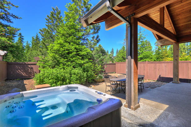 Small fenced  back yard space with dining room table  and hot tub surrounded by trees