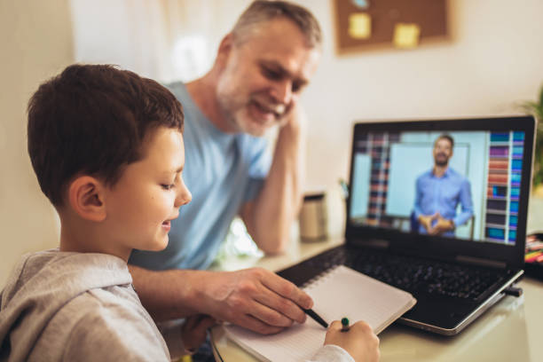 Boy in video conference with teacher on laptop at home. Schoolboy educate online. Father helps his son with home work. Boy in video conference with teacher on laptop at home. home schooling homework computer learning stock pictures, royalty-free photos & images