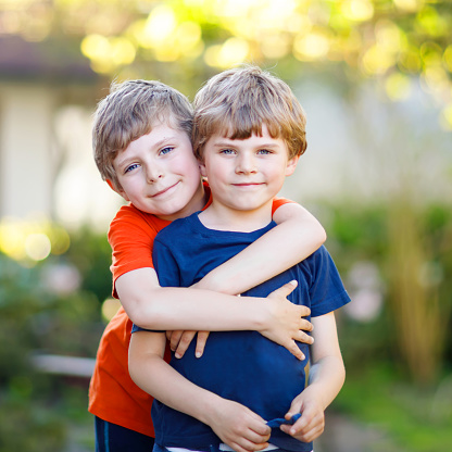 Two little active school kids boys, twins and siblings hugging on summer day. Cute brothers, preschool children and best friends portrait. Family, love, bonding concept.