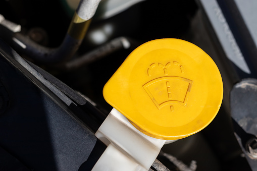 Windshield washer cap. Yellow detail of a car engine compartment under the open hood. Closeup view on a sunny day