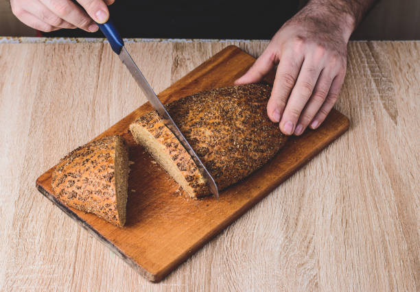 istock A man with a knife cuts bread on a wooden board. 1218993282