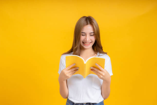 istock Portrait young happy asian woman reading book education studying learning knowledge smiling positive emotion in white t-shirt, Yellow background isolated studio shot and copy space. 1218995174