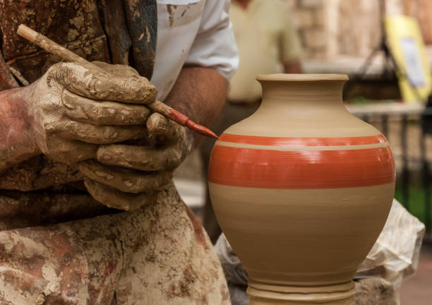 Potter holds a brush to paint a clay vase that rotates on the lathe