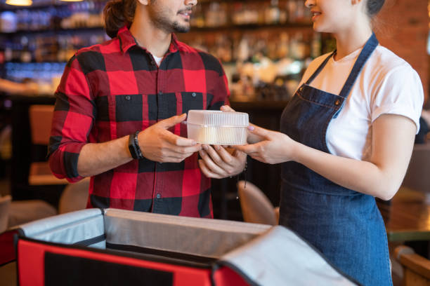 istock Young courier in red flannel taking container with resh food ordered by client 1218997177