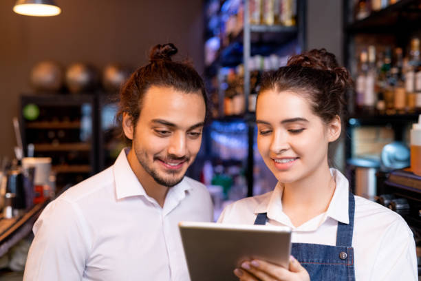 istock Happy young waitress with tablet showing her colleague new points in online menu 1218997189