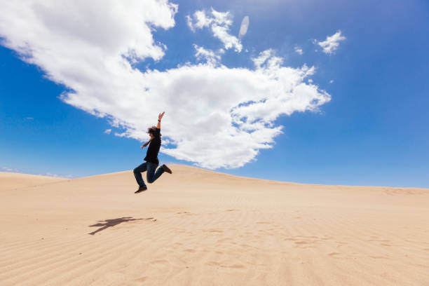 istock Unrecognizable man jumping on the top of a desert dune. 1218998097