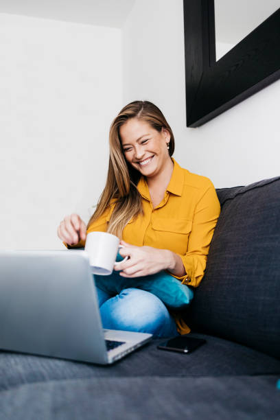 istock Pretty long haired female sitting on sofa with portable computer working remotely from home. 1219002358