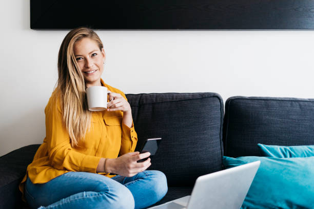 istock Beautiful adult female sitting on sofa while using smartphone 1219002507