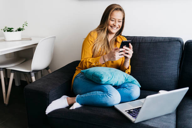 istock Beautiful adult female sitting on sofa while using smartphone 1219002519