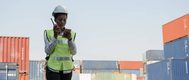 black foreman woman worker working checking at container cargo harbor holding radio walkie-talkie and smartphone to loading containers. african dock female staff business logistics import export shipping concept. - harbor cargo container commercial dock container imagens e fotografias de stock
