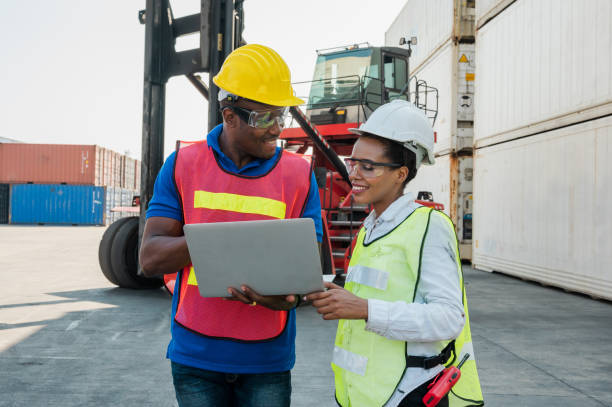 istock Two Black foreman man & woman worker working checking at Container cargo harbor holding laptop computer and using walkie-talkie to loading containers. African dock male and female staff business Logistics import export shipping concept. 1219005903