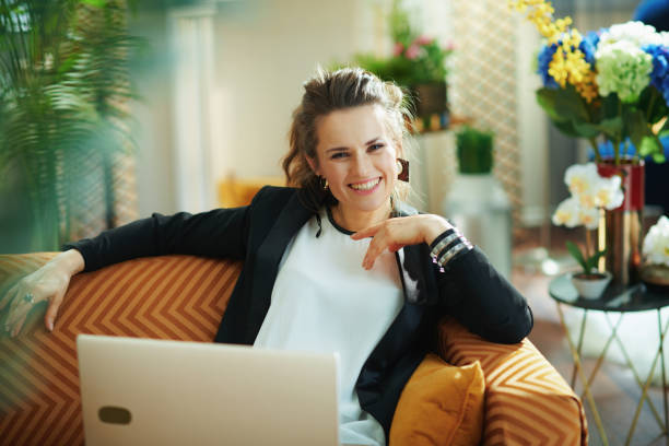 istock smiling elegant female writing on laptop while sitting on couch 1219007746
