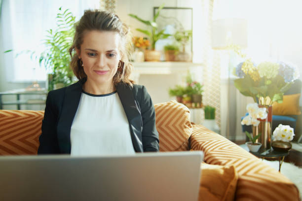 istock trendy housewife writing on laptop while sitting on sofa 1219009223