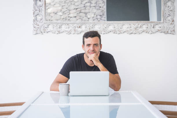 istock Young business manager handsome man with blue eyes sitting on the desktop with computer laptop looking at the camera - luxury lifestyle for caucasian people at home 1219009502