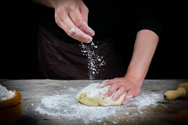 istock Man hands kneading bread dough on a wooden table with black background 1219009879