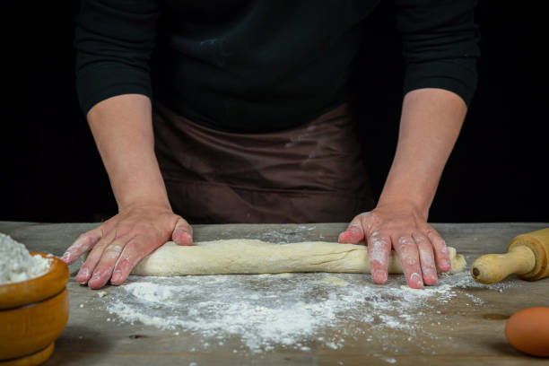 istock Man hands kneading bread dough on a wooden table with black background 1219009888