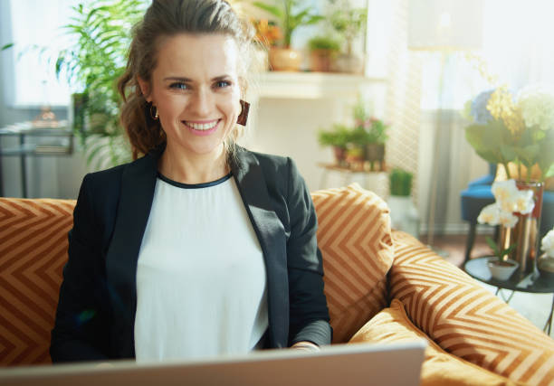 istock happy trendy woman using laptop while sitting on sofa 1219011928