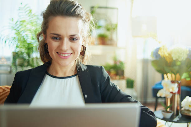 istock happy trendy housewife using laptop while sitting on couch 1219015861