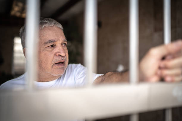 Worried senior man in isolation at home looking through window Worried senior man in isolation at home looking through window prison lockdown stock pictures, royalty-free photos & images