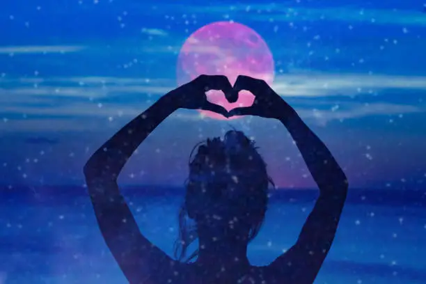 Silhouette of a girl holding heart-shape symbol for love on a starry night sky.