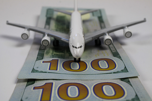 Airplane model on runway of 100 dollar paper money bills (focus on 100)