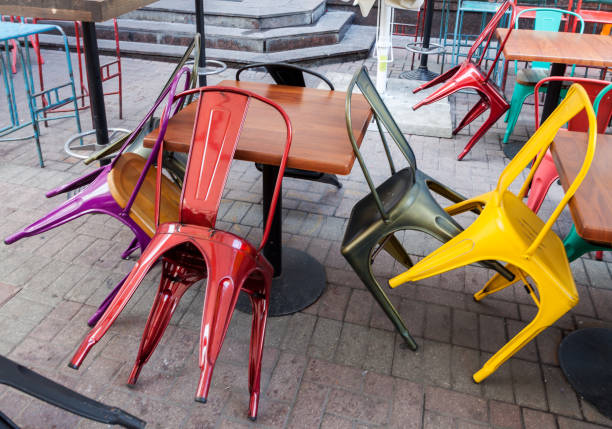 Empty yellow and red upturned chairs and wooden tables closed outdoor sidewalk street cofe. Small business concept