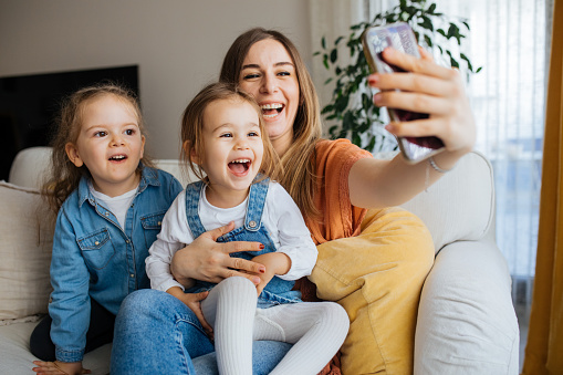 Cheerful mother holding smartphone making selfie with daughters