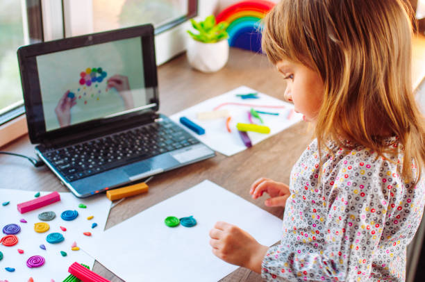 Little girl molding colorful clay cloud with rain watching online learning lesson Little girl molding colorful clay cloud with rain watching online learning lesson on the laptop indoor. Distance home learning concept. motor living stock pictures, royalty-free photos & images
