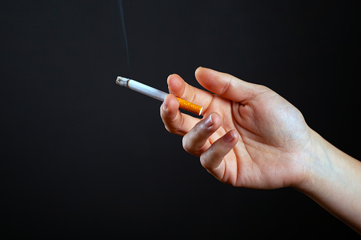 female hand holding a smoking cigarette on a dark background harm from use nicotine close-up.
