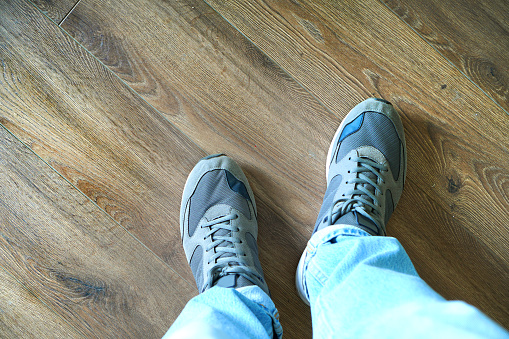 Legs of a man in jeans and sneakers on the laminate floor