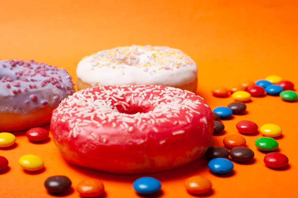 istock three donuts with colorful glaze red white and violet color with scattered chocolates on an orange background. holiday food sweets close-up 1219035251