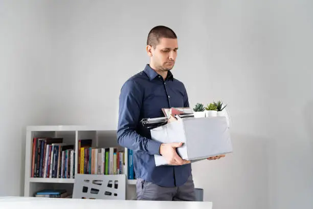 Portrait of adult caucasian man businessman wearing shirt holding a box personal items stuff leaving the office being fired from work due recession economic crisis downturn losing job company shutdown