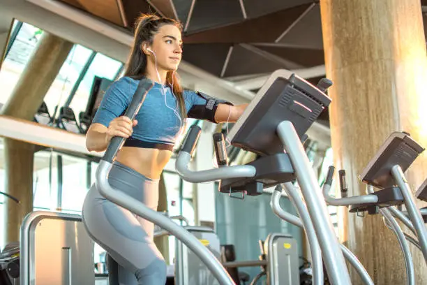 Attractive young fitness woman working out on an elliptical trainer in gym