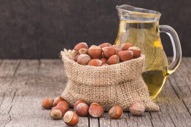 hazelnuts, filbert in burlap sack and hazelnut oil in glass of bottle on wooden backdrop. heap or stack of hazelnuts. hazelnut background, healty food - healty imagens e fotografias de stock