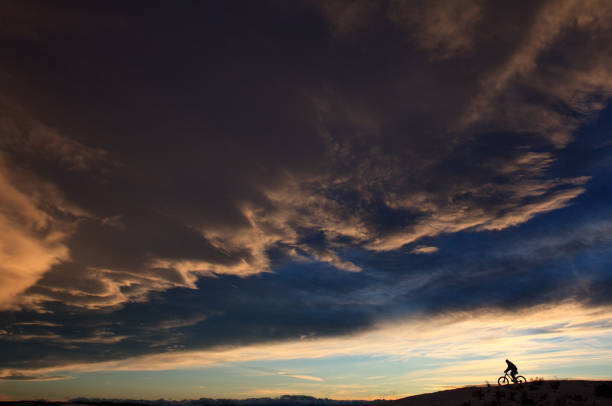 A silhouette of a man mountain biking on a ridge against beautiful ragged sky with chinook cloud in calgary, alberta, Canada.