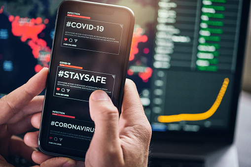 Using #staysafe hashtag for social networking on a smart phone. A hashtag encouraging people to stay home and not risk health due to COVID-19 coronavirus disease. Defocused map with COVID-19 infected countries on the background