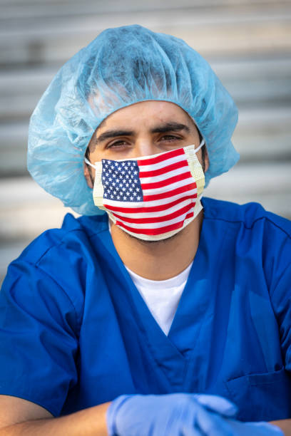 grave surmené, jeune travailleur de santé masculin un masque de protection drapeau américain regardant la caméra - depression sadness usa american flag photos et images de collection