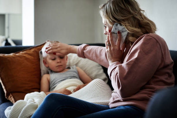 She's calling her doctor for expert medical advice Shot of a mother wearing a surgical mask making a phone call while aiding to her sick young son at home fever stock pictures, royalty-free photos & images