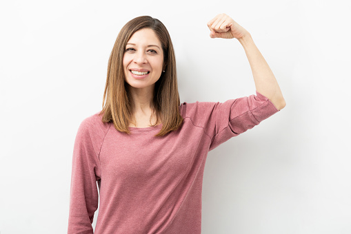 Happy Caucasian woman dressed casual and flexing her arm showing her strength and smiling