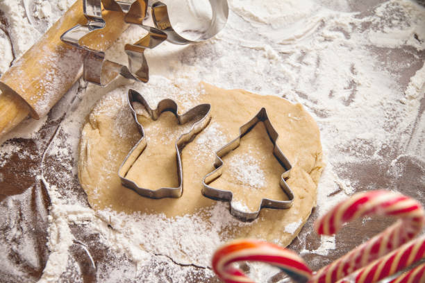 cookie cutters herringbone and angel lie on raw dough with spices for gingerbread on table covered with flour and candy, christmas