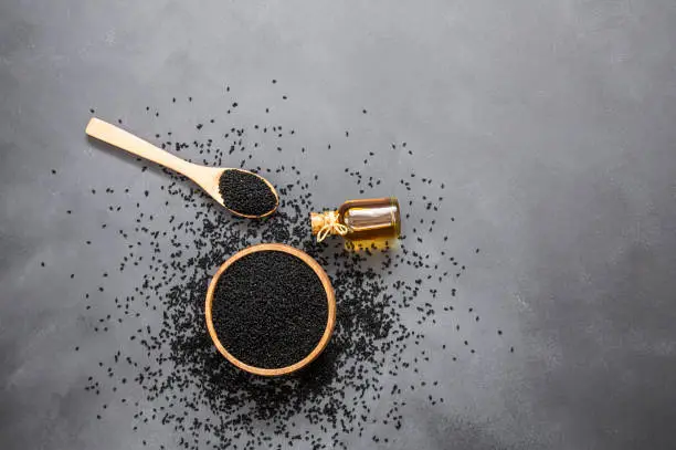 glass bottle of black cumin seeds essential oil , Nigella Sativa in spoon on rustic table. Organic herbal medicine for many diseases, black cumin
