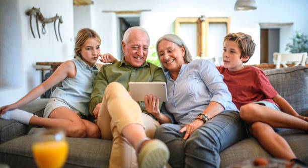 Grandparents and Grandchildren Using Digital Tablet at Home Front view of smiling silver surfer grandparents sitting side by side on couch with preteen grandchildren and using digital tablet. 3610 stock pictures, royalty-free photos & images